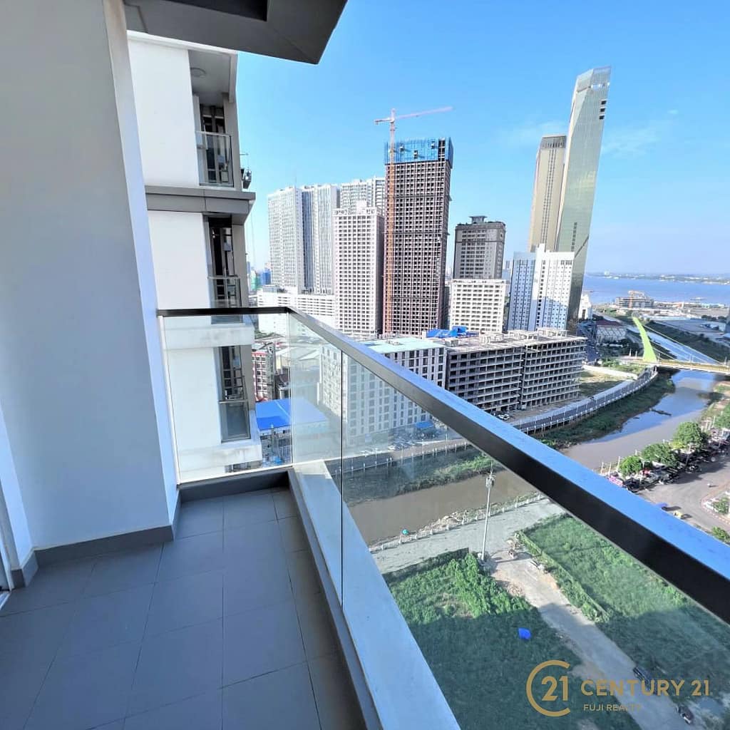A high-rise apartment balcony at Meridian Koh Pich with glass railing overlooks a cityscape of tall buildings, a river, and construction sites under a clear blue sky. Century 21 logo appears in the bottom right corner.