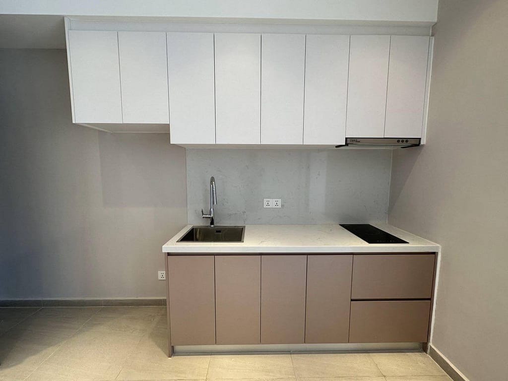 Minimalist kitchen with taupe lower cabinets, white upper cabinets, a built-in sink, electric cooktop, and a sleek time square 3 wall-mounted range hood. The light backsplash and countertop contrast beautifully against the neutral wall.